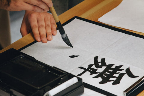 Hand writing a kanji character with a calligraphy brush and black ink