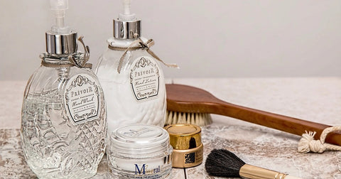 Glass skincare bottles and jars with a wooden brush on a marble surface